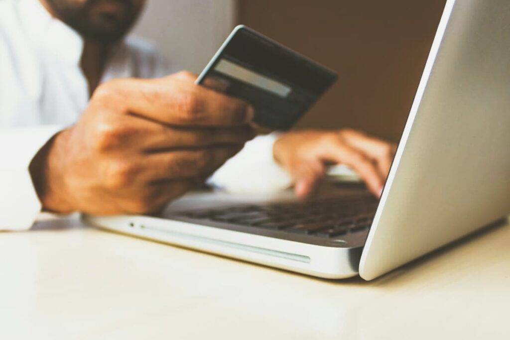 Homem usando um cartão de crédito em frente a um laptop, representando a compra online e transações digitais.
