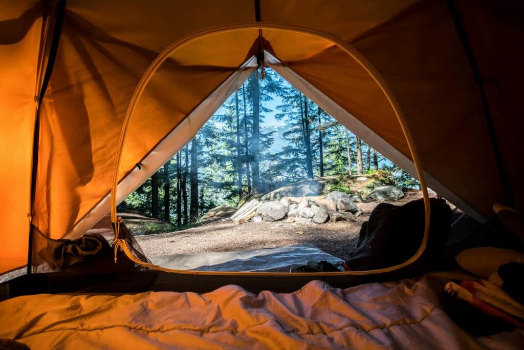 Vista de uma tenda em um acampamento, com árvores e uma pedreira ao fundo, ideal para atividades ao ar livre e contato com a natureza.