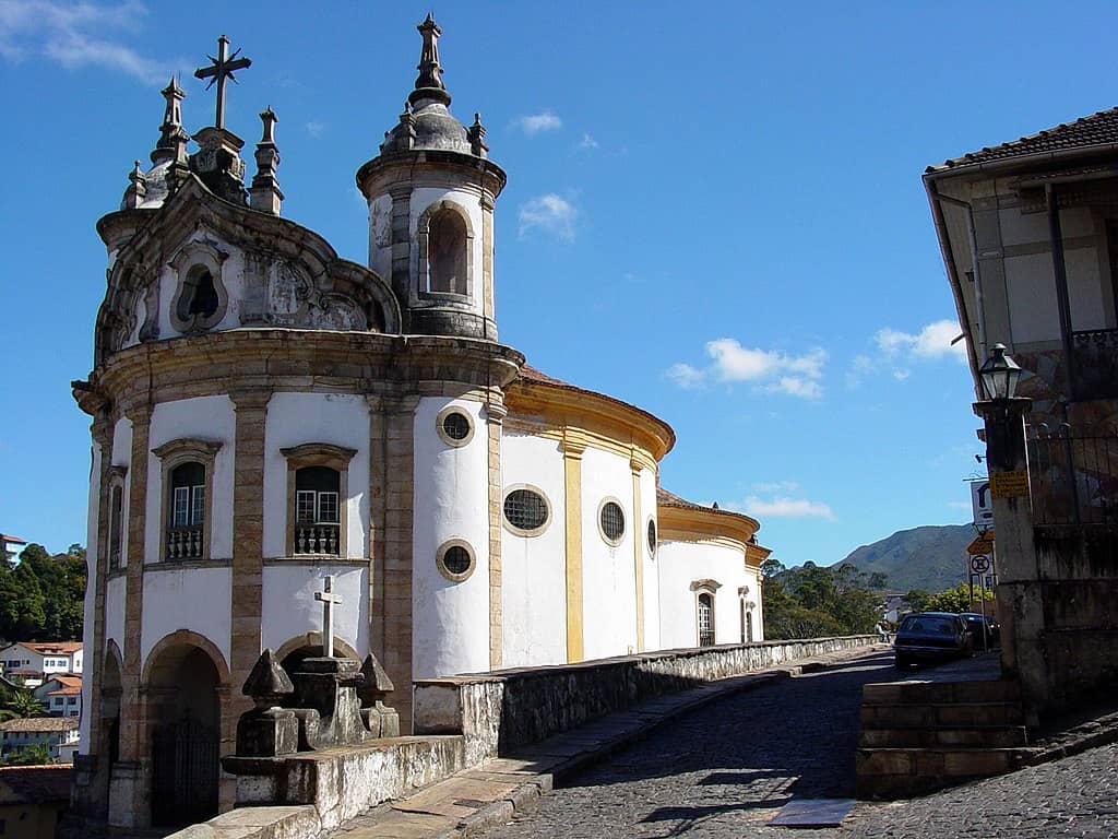 Vista panorâmica da Igreja de São Francisco de Assis, em Ouro Preto, com céu azul e cercada por casas coloniais. Destaca a arquitetura barroca.